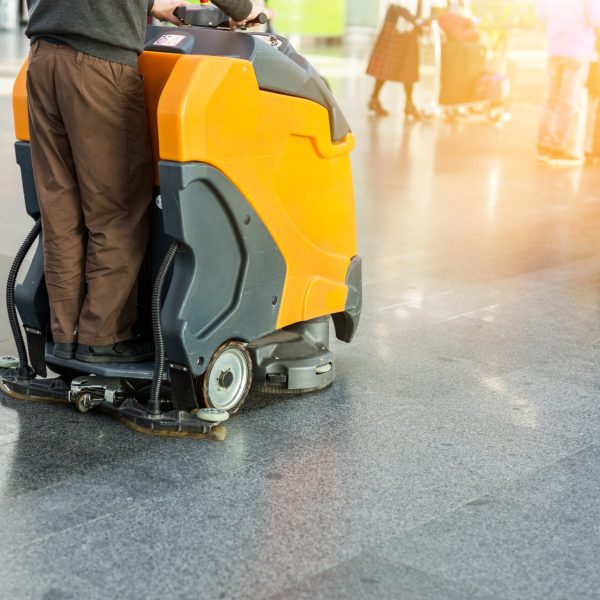 Man driving professional floor cleaning machine at airport or railway station.  Floor care and cleaning service agency.